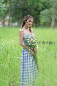 蓝格裙少女怀抱野花立于青翠草丛中