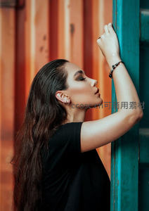 倚靠彩色集装箱的沉思女子侧影