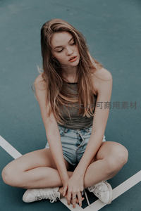 少女盘腿坐球场低头沉思