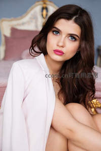 棕发蓝眼少女坐床边，粉色西装尽显温柔知性