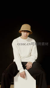 米色渔夫帽少年，纯白上衣配黑裤坐姿随性