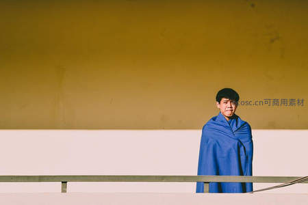 蓝毯裹身男子伫立黄色墙前