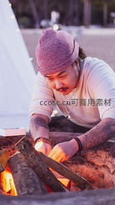 篝火旁纹身男专注添柴露营