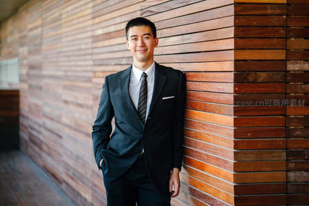 西装青年倚靠木质墙面微笑