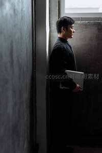 职场男士倚墙，手握笔记本电脑