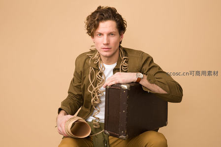 卷发男子怀抱旧皮箱手持纸筒