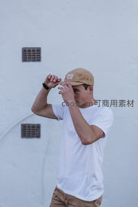 白墙前男子调整卡其色棒球帽