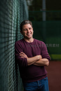 中年男子球场边微笑抱臂倚网