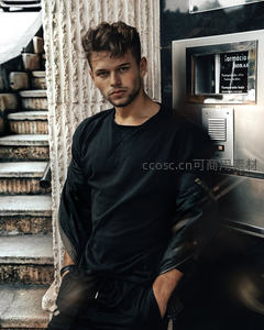 街头潮男倚墙而立，现代建筑映衬酷帅造型