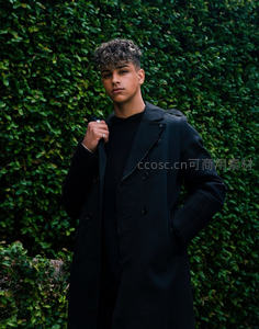 绿植墙前的时尚青年，黑色风衣尽显帅气