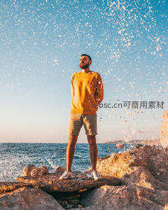 海边岩石上沐浴海浪飞沫的黄衣男子