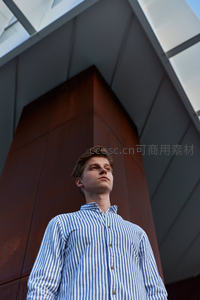条纹衬衫青年仰望现代建筑，低角度构图
