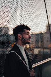 带纹身的潮男倚靠铁网眺望城市日落