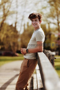 阳光下微笑的年轻男子倚靠木栏