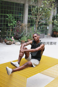 黑人青年坐于黄色网格长凳之上