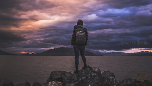 背包客立于礁石之上，远眺风云变幻的湖光山色
