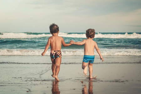 两个孩子手牵手在海边奔跑嬉戏