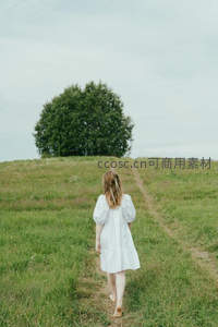 白衣女子赤足走向山坡孤树