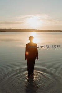 西装男子伫立湖面沐浴金色夕阳