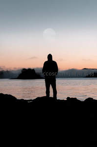 剪影人立岩石迎日落月升时刻