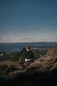 孤身女子静坐山顶俯瞰城市与海湾