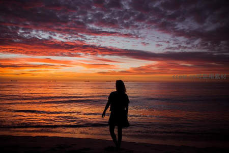 海边漫步身影融入橙红落日余晖之中