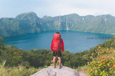 背包客伫立山巅，俯瞰碧绿火山湖