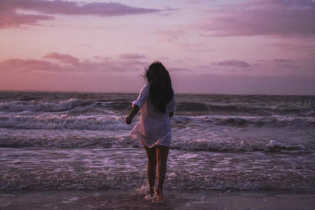 海边少女奔跑于粉紫夕阳浪花间