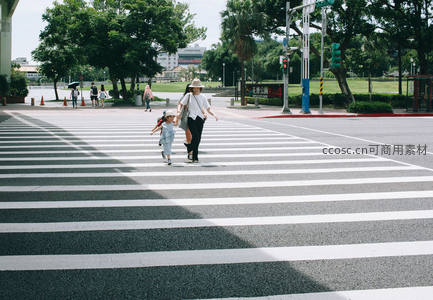 母子牵手过马路，绿树成荫公园旁的温馨瞬间