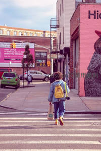 孩童背黄书包过马路，涂鸦墙与城市街景相映成趣