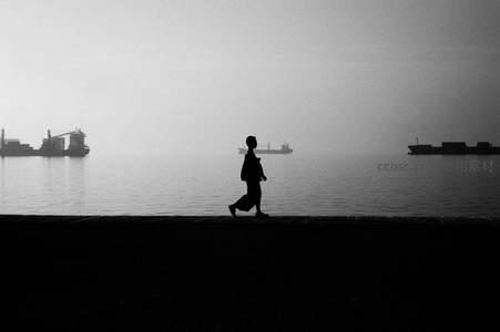 剪影行人独行海边，远处货轮静泊雾中
