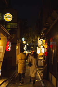 夜色中情侣漫步日式小巷，暖灯映衬浪漫氛围