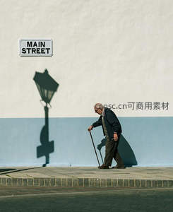 老者拄杖缓行主街墙影相伴