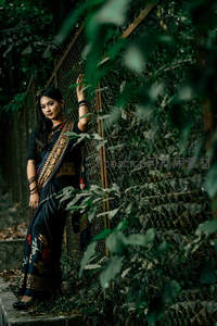 黑纱丽女子倚栅栏，绿叶掩映静美