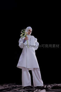 白衣女子手捧鲜花立于暗幕