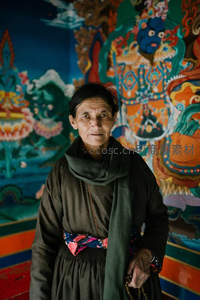 藏族老妇人站在色彩斑斓的唐卡前