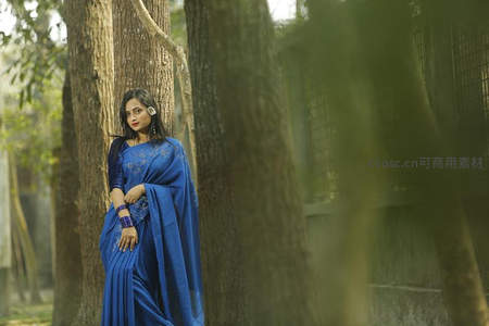 蓝纱丽女子倚树而立，林间光影温柔静谧