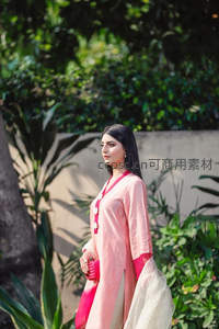 粉衣女子手持小包漫步庭院绿荫