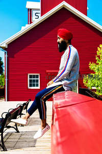 红帽男子坐于红色谷仓前木凳