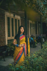 身着黄纱丽的女子在绿植庭院中回眸