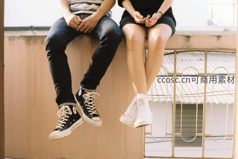 情侣并肩坐墙头，脚悬空中显青春活力