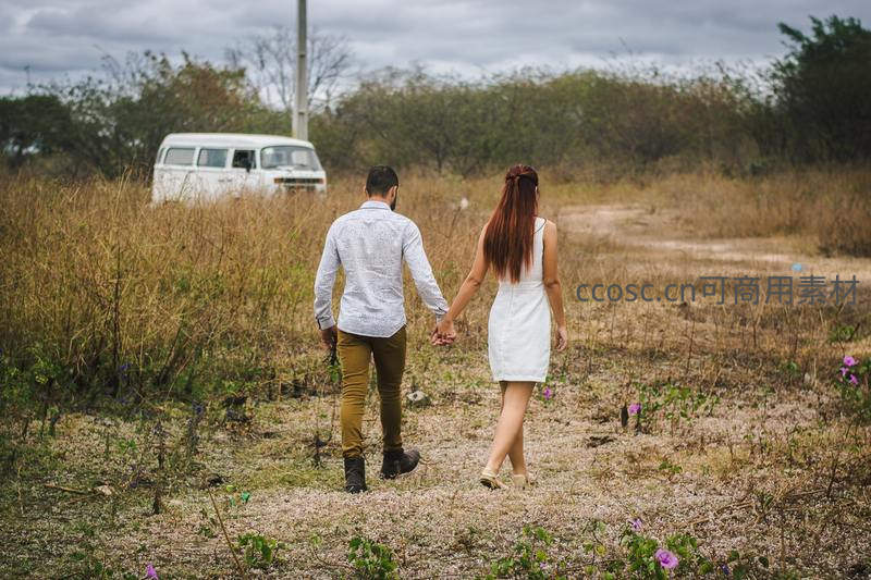 情侣牵手漫步荒野小径，复古面包车静候远方