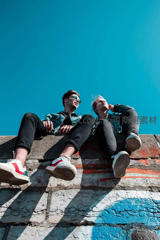 蓝天下的年轻情侣坐在涂鸦墙边