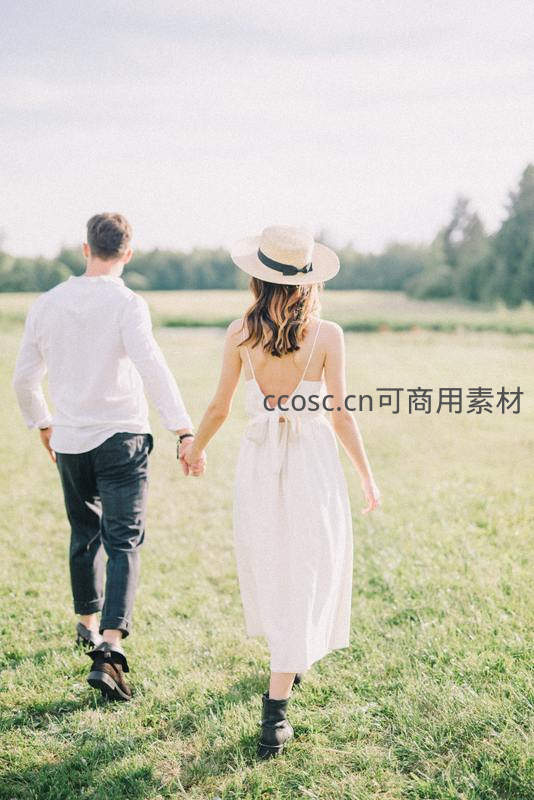 牵手漫步绿野，白衣情侣背影如诗