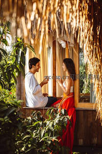 茅草屋下情侣对坐品茗，阳光洒落温馨惬意