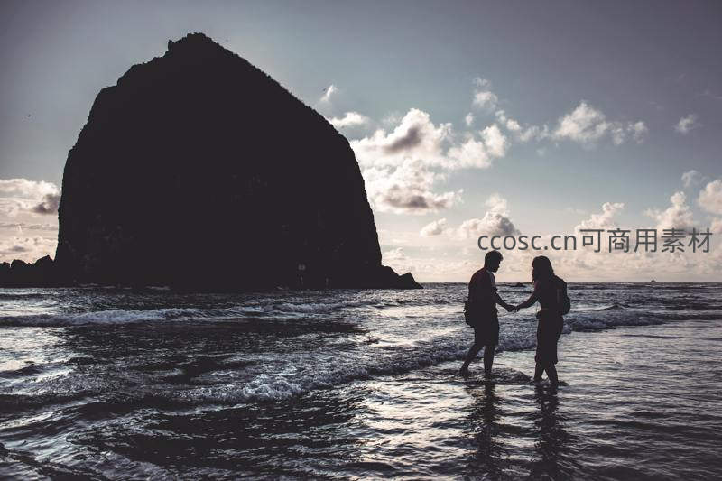 海边剪影下，恋人携手踏浪共赏巨岩