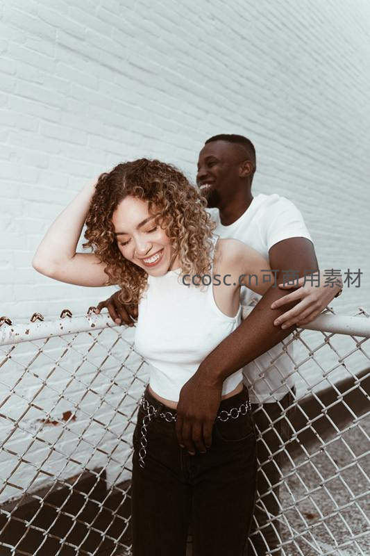 情侣依偎在白色砖墙前的温馨瞬间