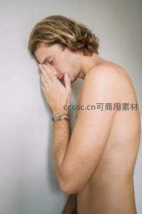 赤裸上身男子靠墙闭眼手捂脸显疲惫或沉思
