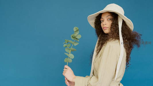 卷发女子戴帽持桉树叶凝视