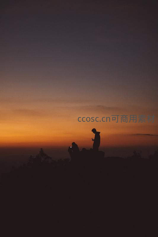山顶剪影下欣赏日落的旅人